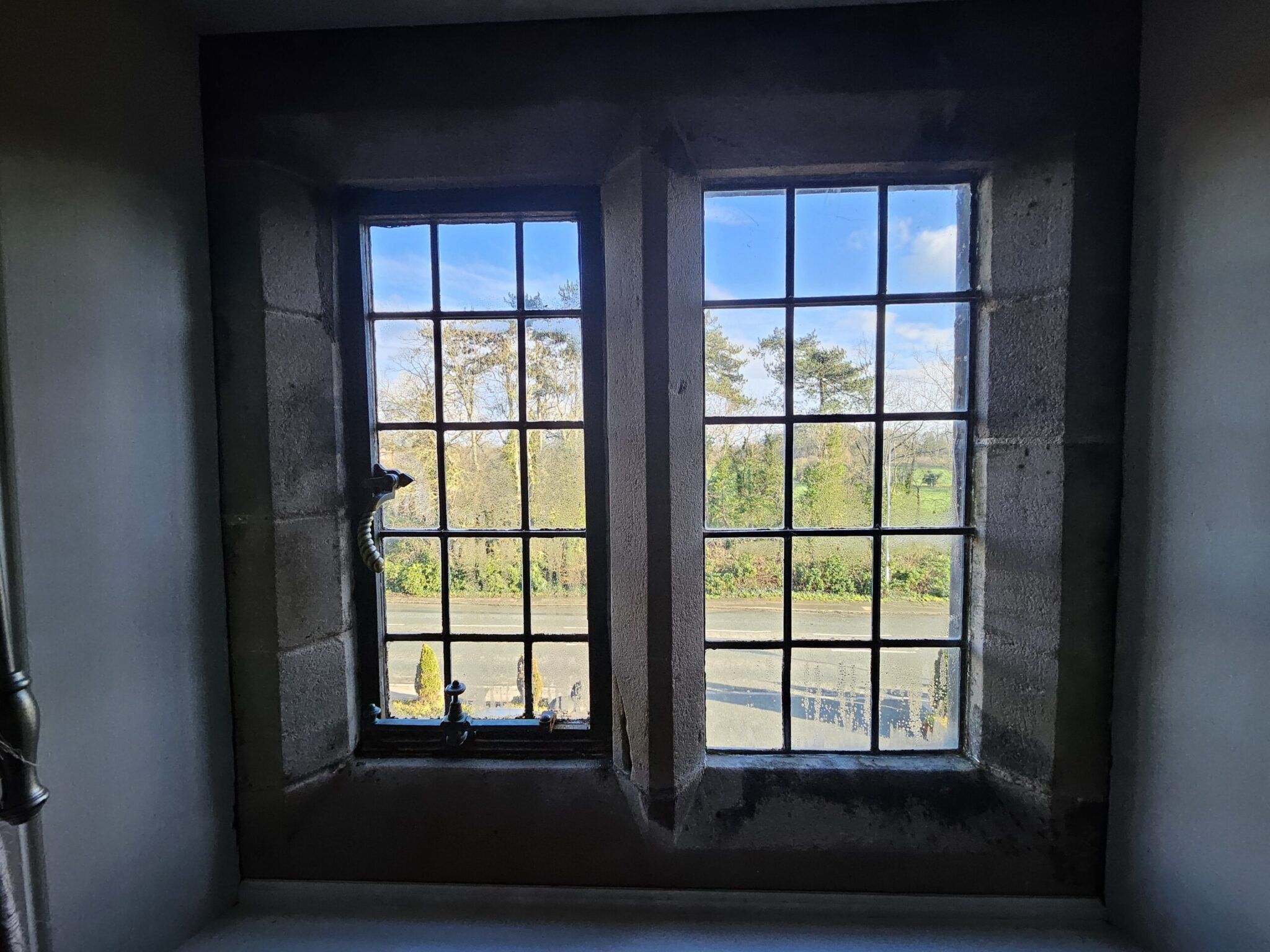 Stone-framed leaded window with a view of a country road, hedges, trees and blue sky
